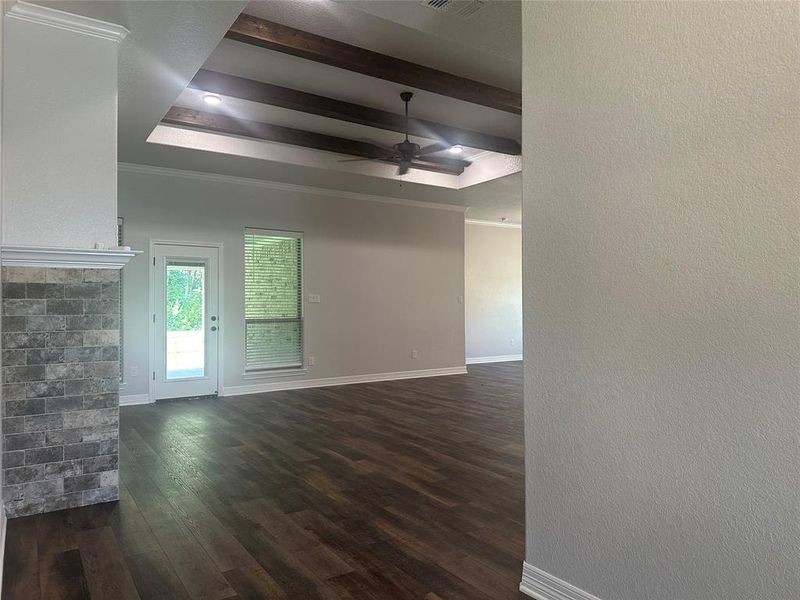 Unfurnished living room with a raised ceiling, dark wood-style floors, a ceiling fan, beamed ceiling, and crown molding