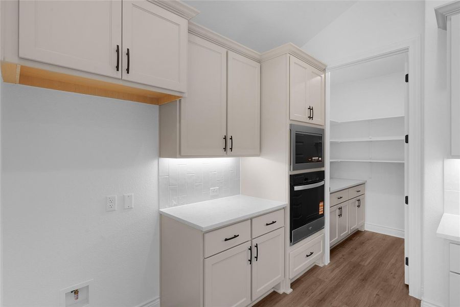 Kitchen with stainless steel appliances, dark wood finished floors, vaulted ceiling, white cabinets, and light stone counters