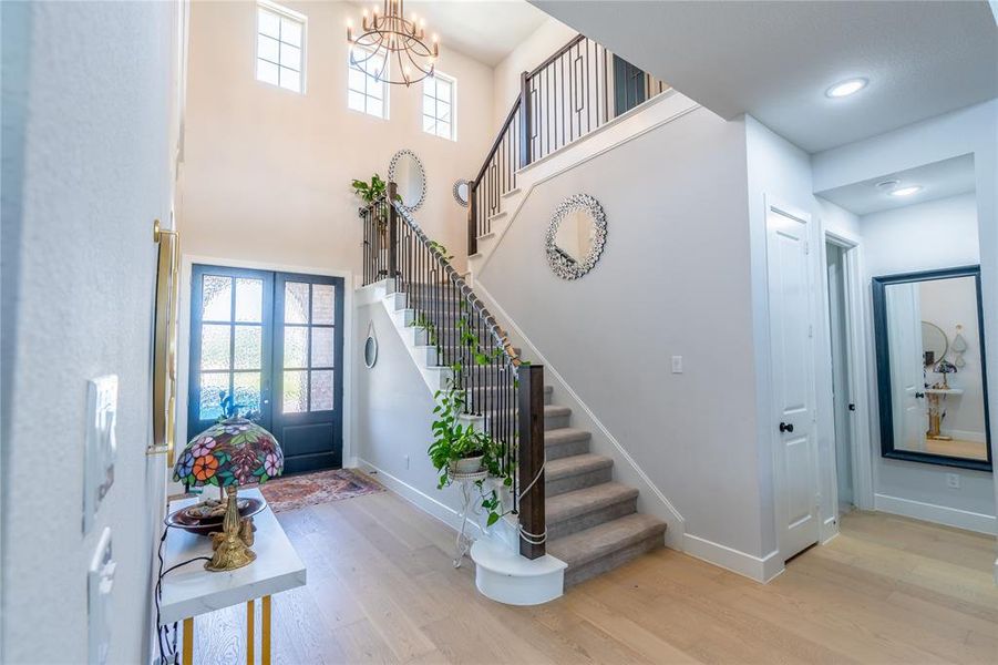 Foyer featuring light wood-style flooring, stairway, french doors, a chandelier, and a towering ceiling