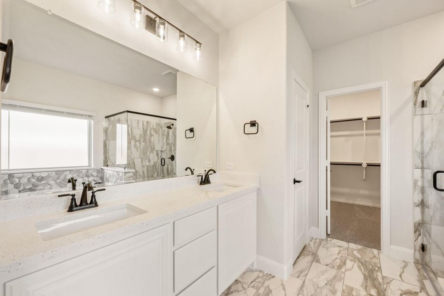 Master bathroom with double vanity, white quartz countertops, marble tile floors, and glass shower with walk-in closet entry