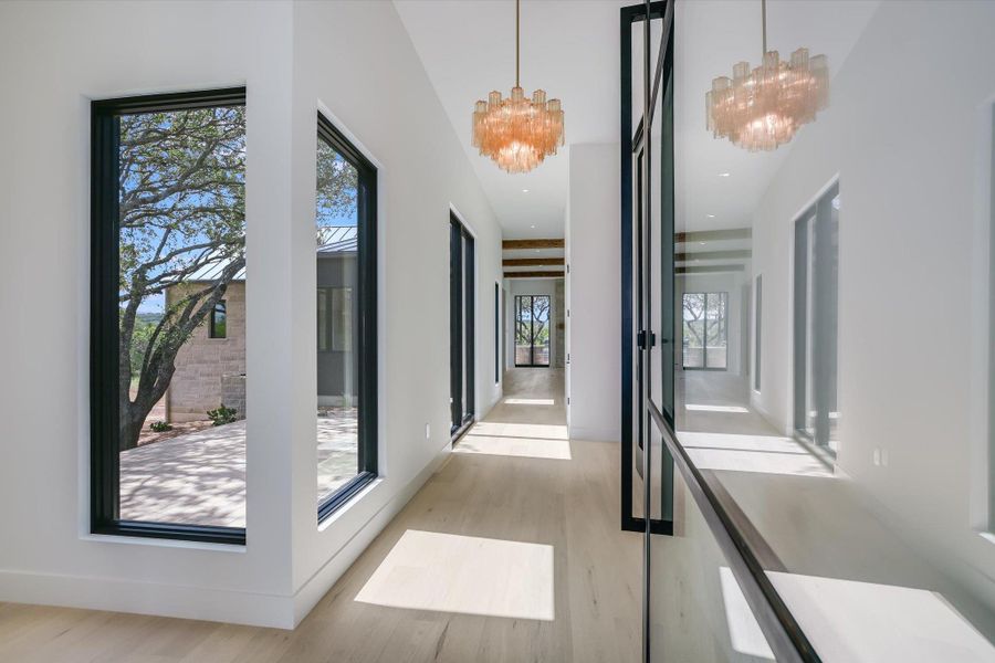 A well-lit corridor boasts striking chandeliers and ample natural light through tall windows.