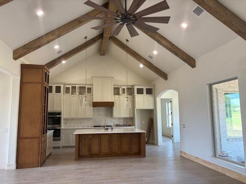 Kitchen with a large island, glass insert cabinets, high vaulted ceiling, arched walkways, and brown cabinetry