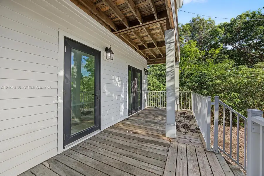 Covered wooden deck featuring horizontal siding, glass-panel exterior doors, painted square columns, and metal railings Covered wooden deck featuring horizontal siding, glass-panel exterior doors, painted square columns, and metal railings