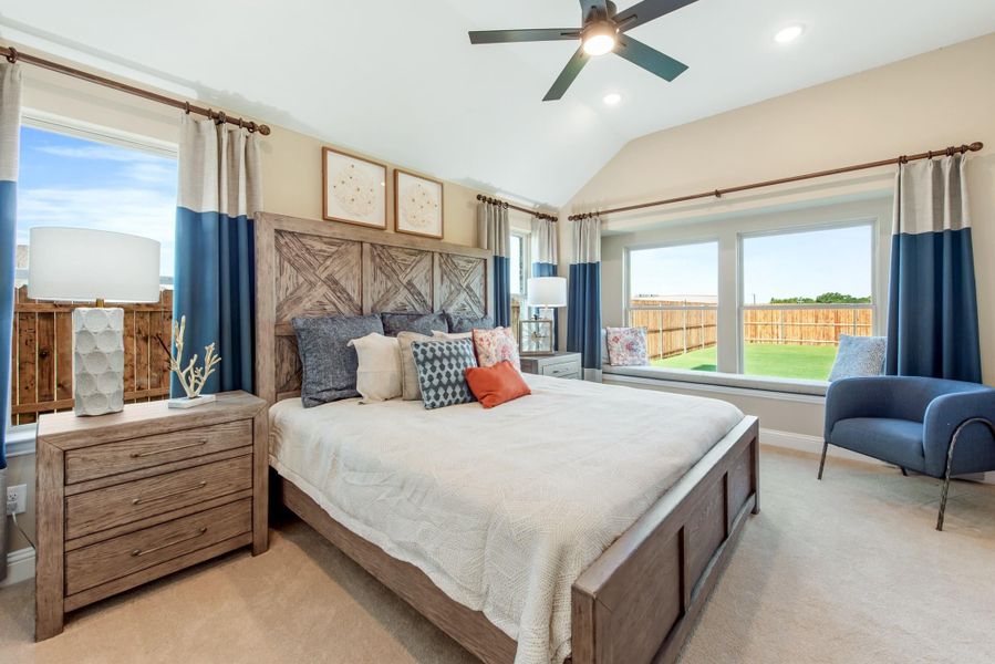 Bedroom with vaulted ceiling, wood headboard, ceiling fan, and large windows with blue curtains Bedroom with vaulted ceiling, wood headboard, ceiling fan, and large windows with blue curtains