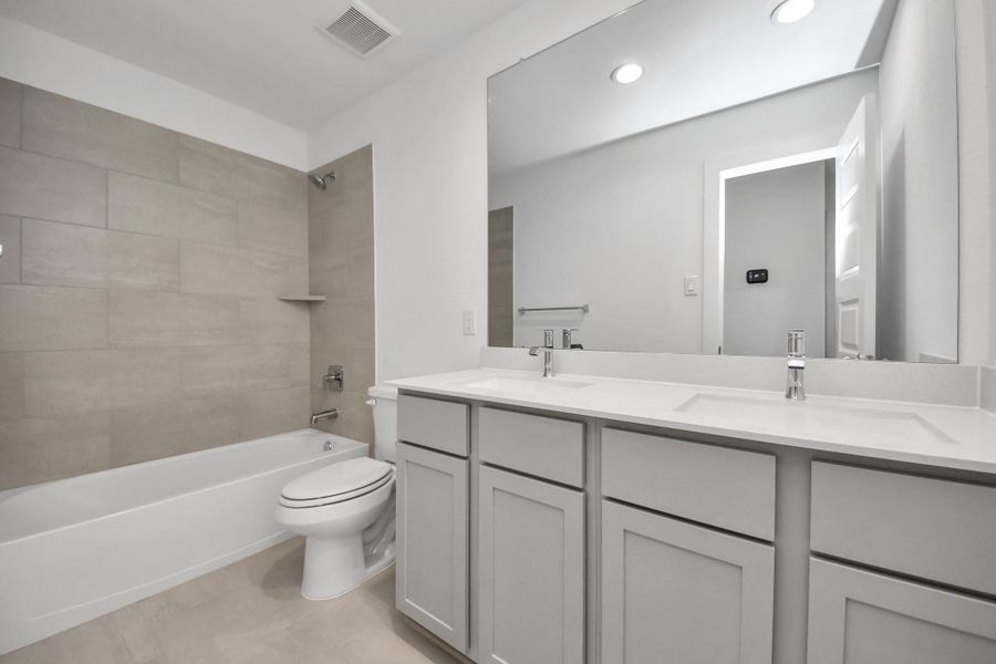 Secondary bath features tile flooring, bath/shower combo with tile surround, light stained wood cabinets, beautiful light countertop. Sample photo of completed home with similar floor plan. Actual colors and selections may vary.