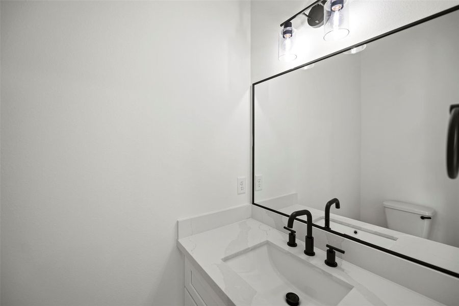 Modern half bathroom with a sleek white vanity, black fixtures, a large mirror, and bright lighting.