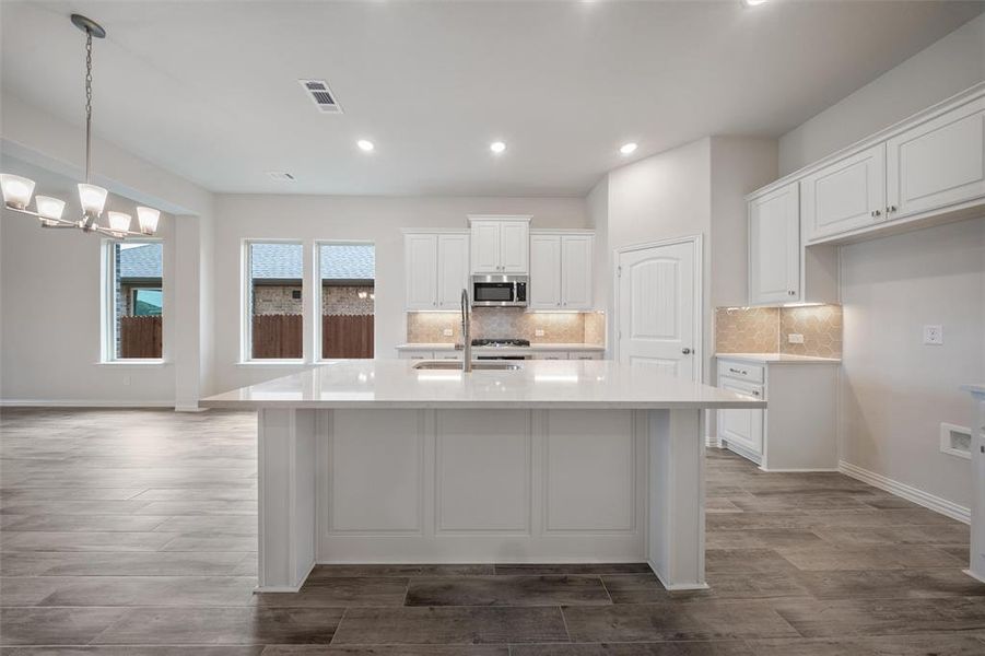 Kitchen featuring wood finished floors, white cabinets, a center island with sink, decorative backsplash, and recessed lighting