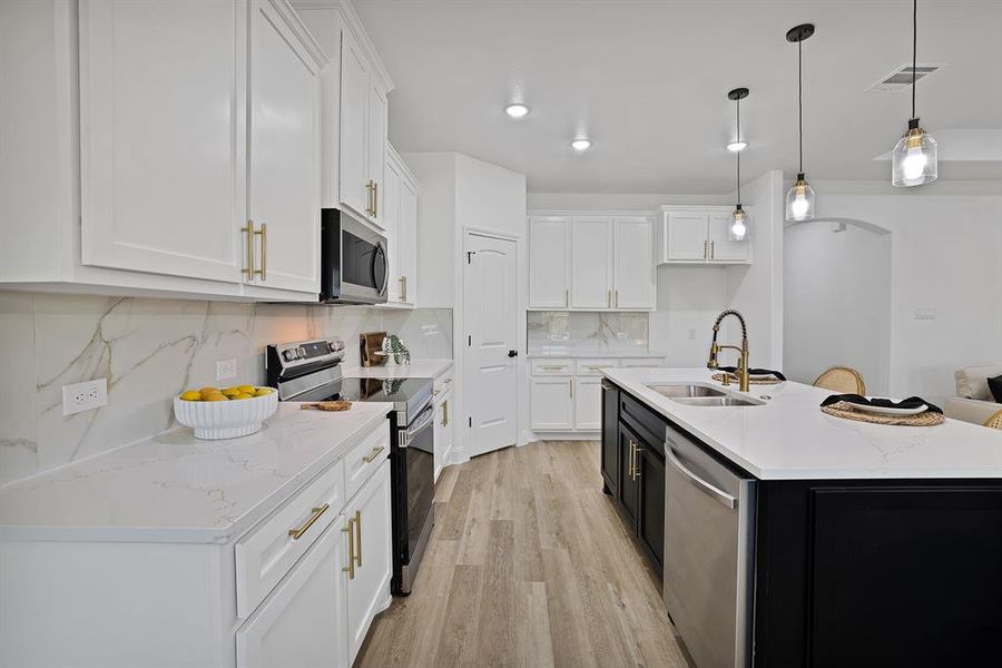 Kitchen featuring white cabinets, appliances with stainless steel finishes, a center island with sink, and sink