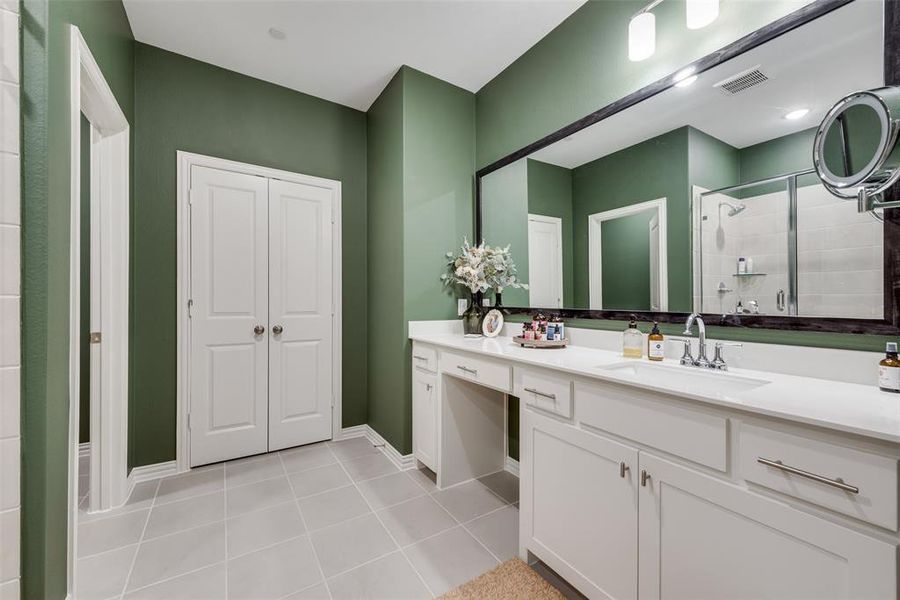 Bathroom featuring a dual vanity with white cabinetry and integrated sinks, an upgraded large framed mirror, a separate shower with glass enclosure, and light tile flooring Bathroom featuring a dual vanity with white cabinetry and integrated sinks, an upgraded large framed mirror, a separate shower with glass enclosure, and light tile flooring