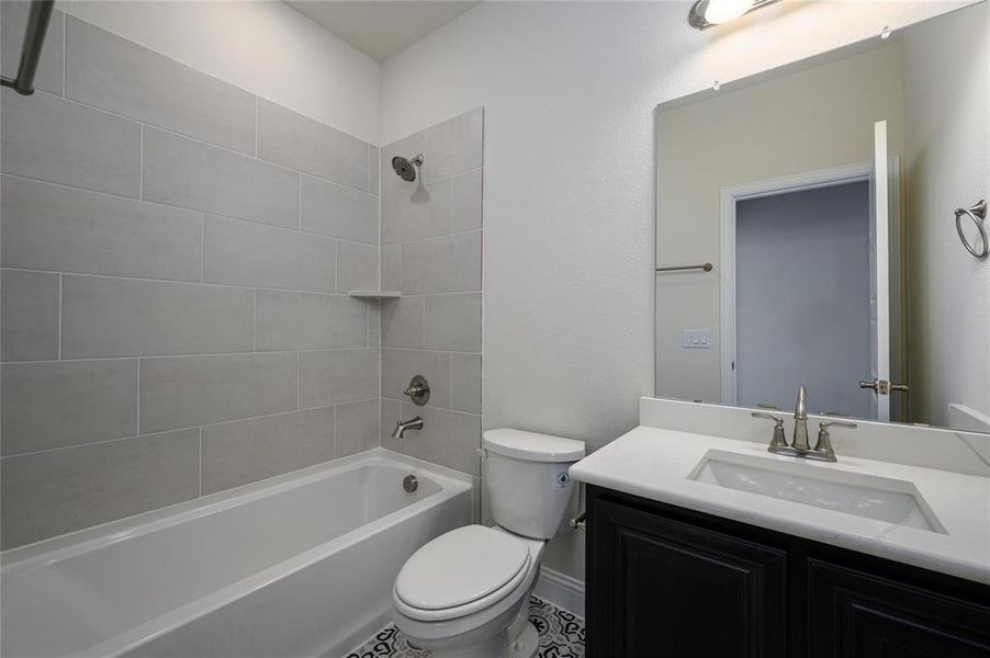 Full bathroom with vanity, tiled shower / bath combo, toilet, and tile patterned flooring