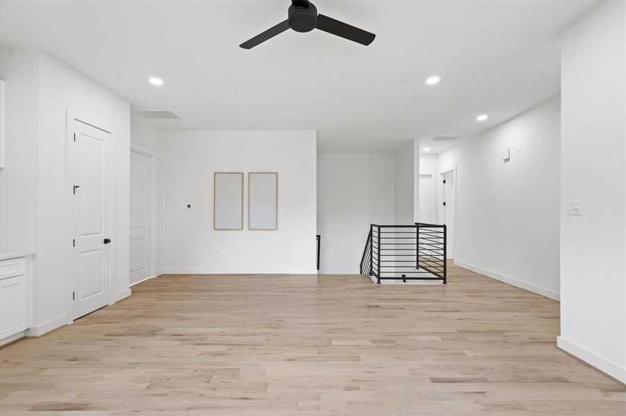 Spacious second-floor game room with wood flooring, recessed lighting, ceiling fan, and elegant white built-ins.