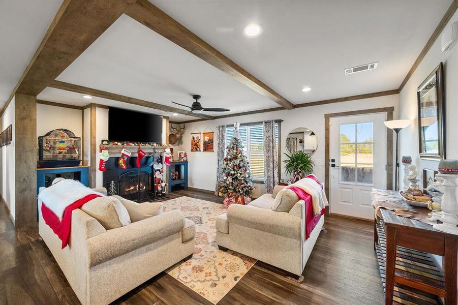 Living area featuring wood-finish flooring, exposed ceiling beams, recessed lighting, and a dark-toned fireplace with an integrated mantel