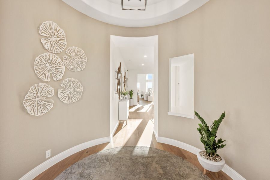 Circular foyer with domed ceiling, decorative wall art, potted plant, and hallway leading to living area