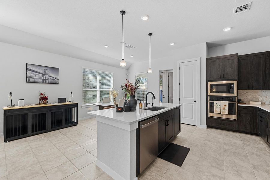Kitchen with pendant lighting, appliances with stainless steel finishes, a center island with sink, light stone countertops, and light tile patterned flooring