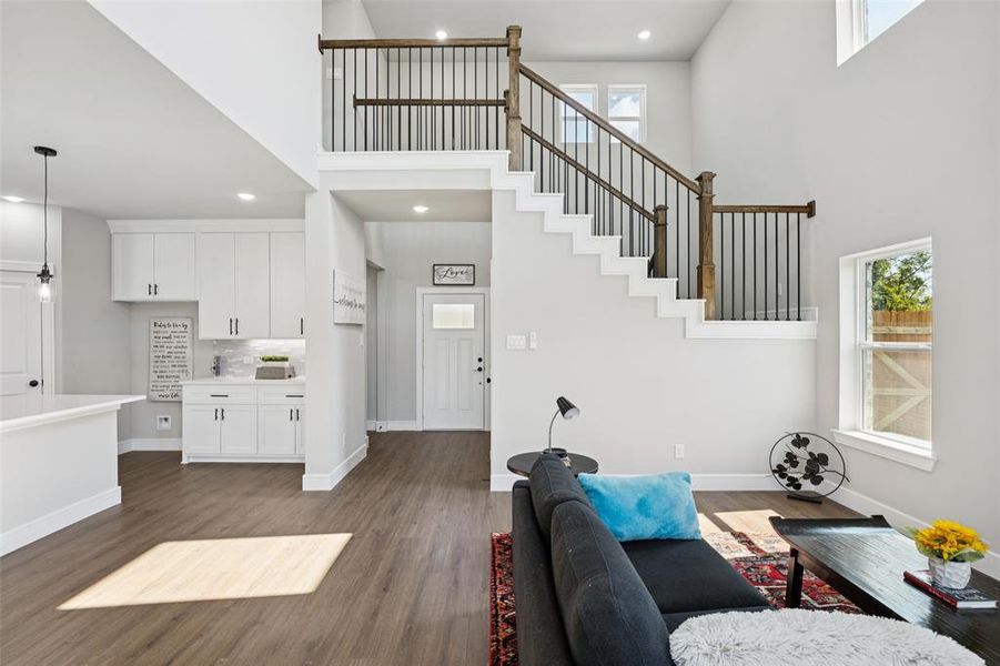 Living area featuring a towering ceiling, healthy amount of natural light, dark wood-style flooring, recessed lighting, and stairs