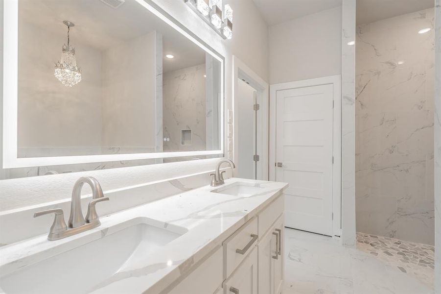 Bathroom featuring light marble finish flooring, double vanity, a marble finish shower, and a chandelier