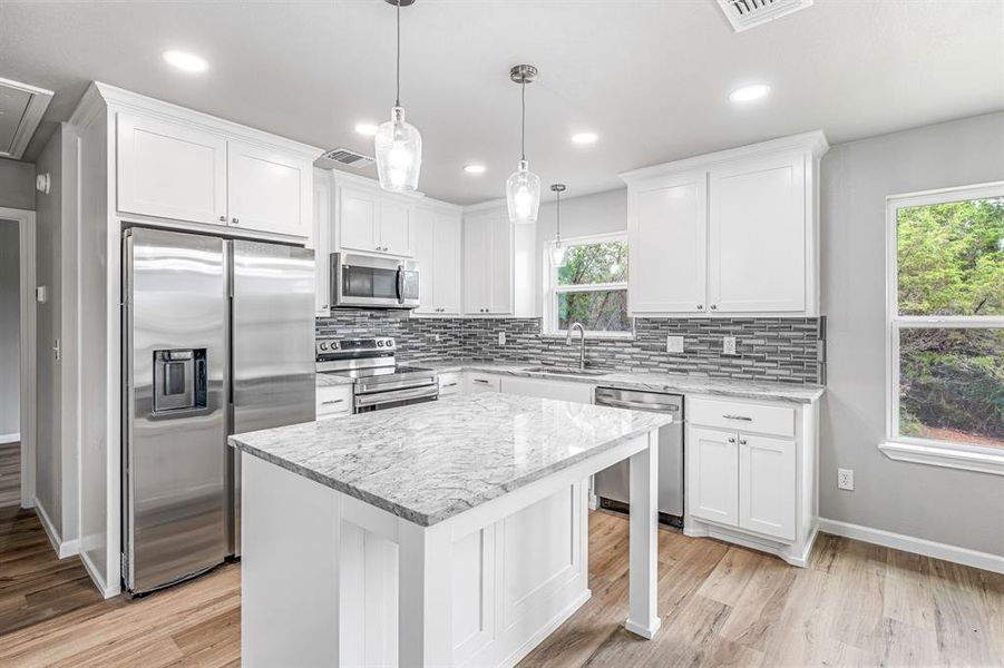 Kitchen featuring stainless steel appliances, a sink, backsplash, white cabinetry, and light wood finished floors Kitchen featuring stainless steel appliances, a sink, backsplash, white cabinetry, and light wood finished floors