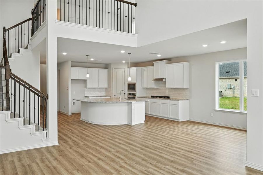 Kitchen with white cabinetry, light wood-type flooring, a high ceiling, tasteful backsplash, and a center island with sink Kitchen with white cabinetry, light wood-type flooring, a high ceiling, tasteful backsplash, and a center island with sink
