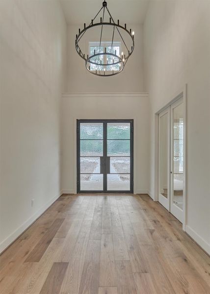 Grand foyer with soaring ceilings, a statement chandelier, and striking glass double doors that flood the space with natural light.