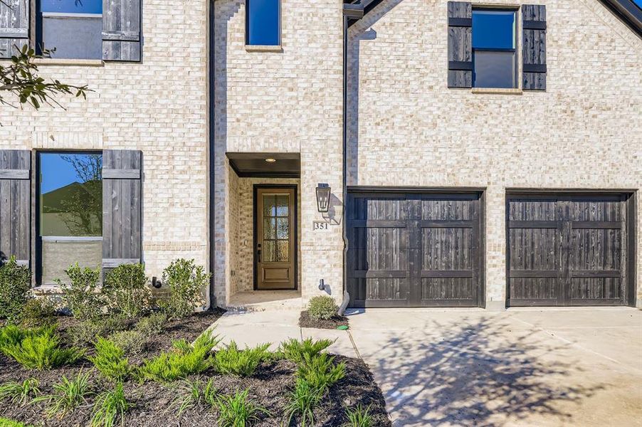 Doorway to property featuring driveway, brick siding, and an attached garage