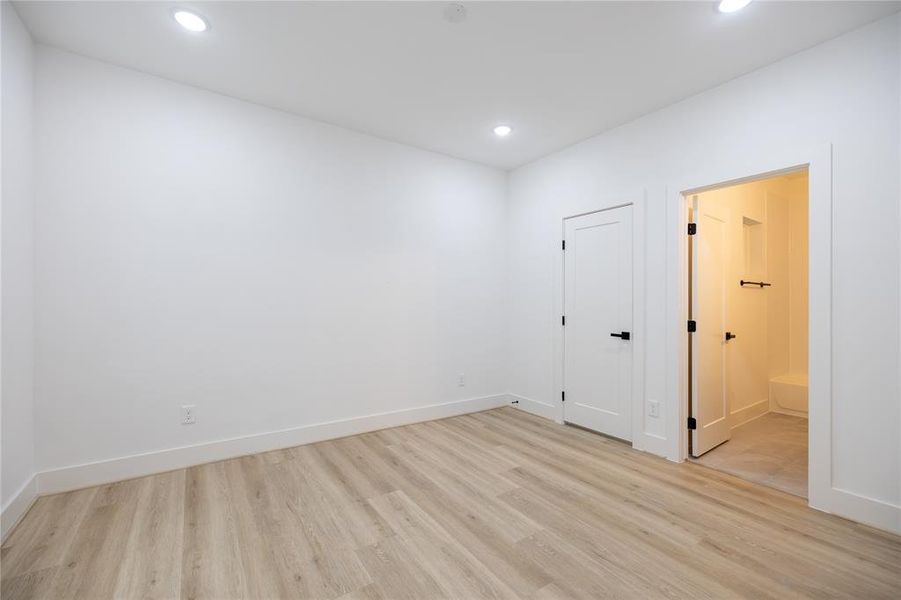 The spacious first-floor bedroom showcases wood-like LVP flooring, recessed lighting, and a large window that bathes the room in natural light.