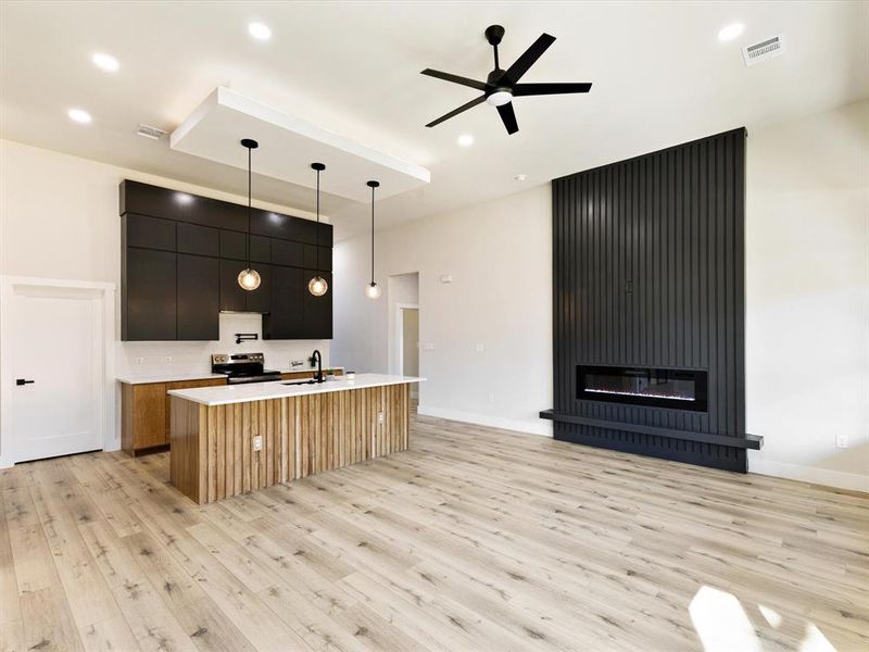 Kitchen featuring an island with sink, modern cabinets, decorative light fixtures, a fireplace, and light wood-type flooring