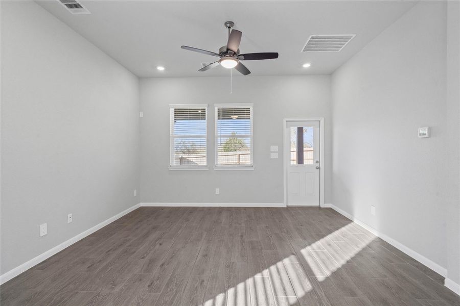 A bright and airy open-concept space featuring LVP flooring, high ceilings with recessed lighting and ceiling fan, abundant natural light from large windows (fitted with blinds), and an access door to the back covered patio.