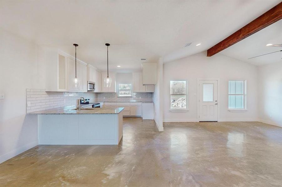 Kitchen featuring kitchen peninsula, decorative backsplash, stainless steel appliances, lofted ceiling with beams, and white cabinetry