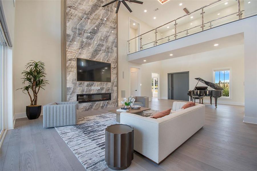 Living area featuring a high end fireplace, wood finished floors, a high ceiling, a ceiling fan, and recessed lighting Living area featuring a high end fireplace, wood finished floors, a high ceiling, a ceiling fan, and recessed lighting