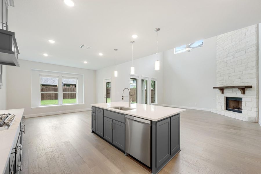 Open kitchen with gray island, white countertops, and stone fireplace in adjoining living area Open kitchen with gray island, white countertops, and stone fireplace in adjoining living area