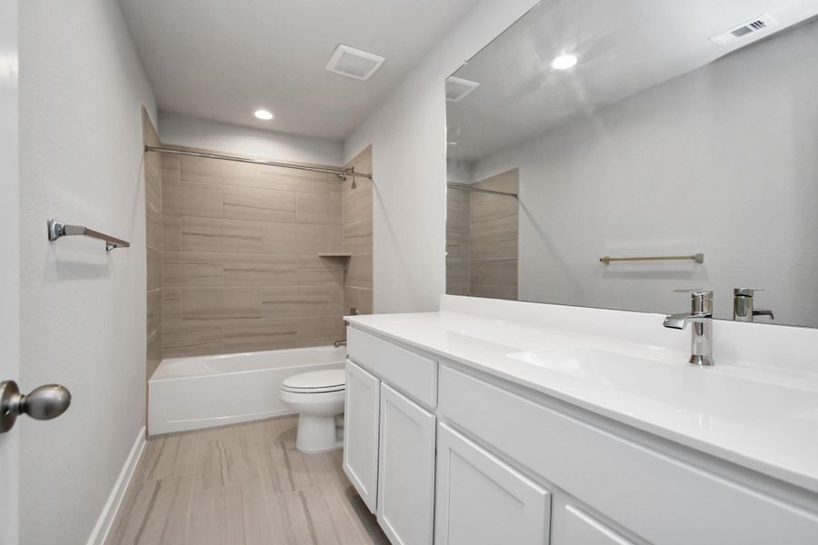 The secondary bath includes modern tile flooring, a combined bath and shower with a tile surround, light wood cabinetry, and a beautiful light-colored countertop. Sample photo of completed home with similar floor plan. Actual colors and selections may vary. The secondary bath includes modern tile flooring, a combined bath and shower with a tile surround, light wood cabinetry, and a beautiful light-colored countertop. Sample photo of completed home with similar floor plan. Actual colors and selections may vary.