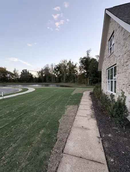 Brick exterior featuring a concrete walkway, expansive lawn, and pond frontage