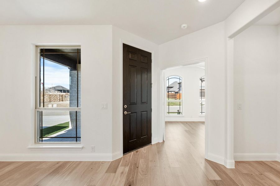 Entryway with dark wood front door, light hardwood floors, and large windows with neighborhood views Entryway with dark wood front door, light hardwood floors, and large windows with neighborhood views