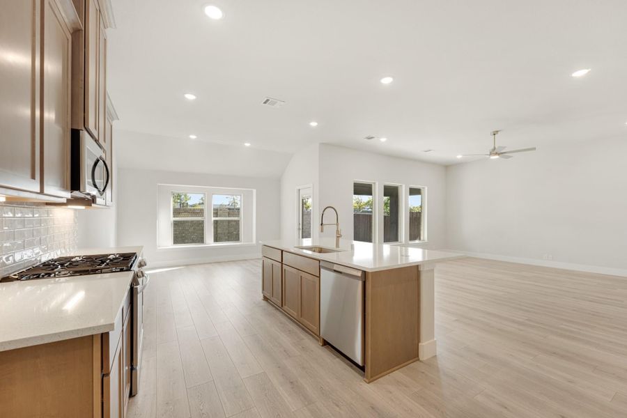 Open-concept kitchen with wood cabinets, center island with sink, and light hardwood floors opening to living area Open-concept kitchen with wood cabinets, center island with sink, and light hardwood floors opening to living area