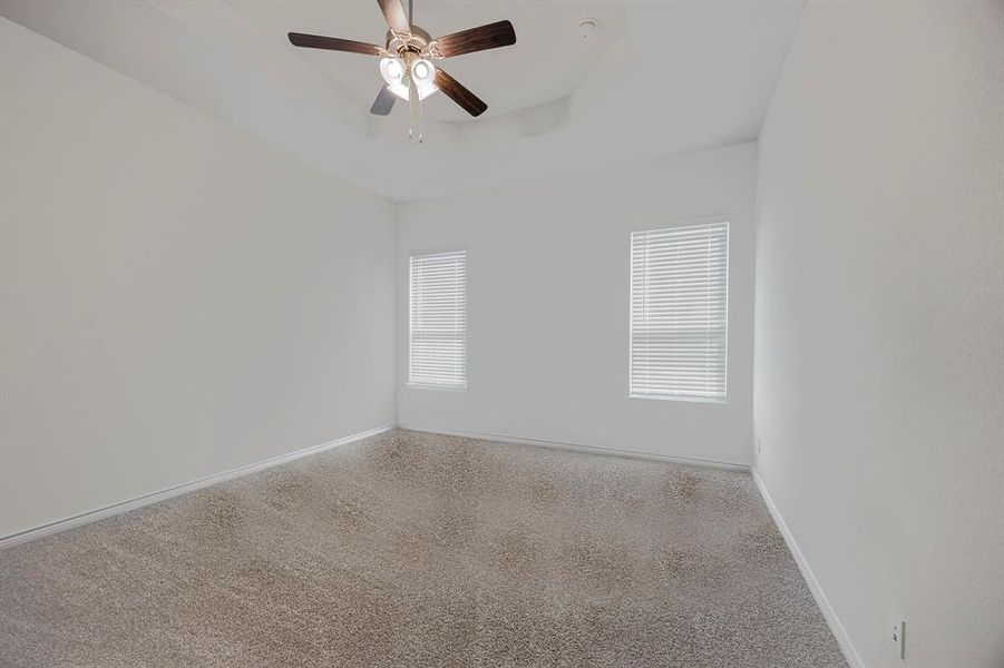 Empty room featuring a tray ceiling, carpet flooring, and ceiling fan