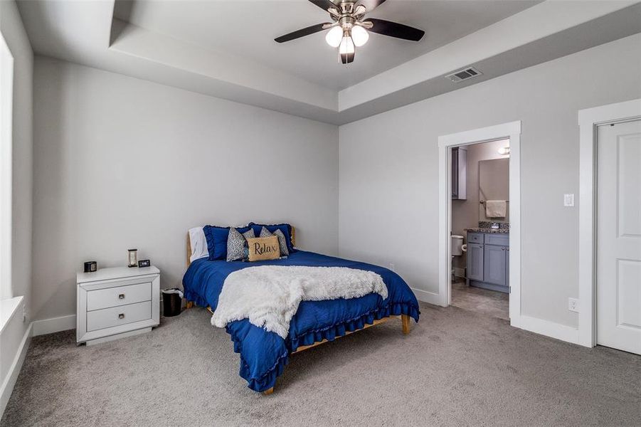 Bedroom featuring a raised ceiling, light carpet, a ceiling fan, and ensuite bath