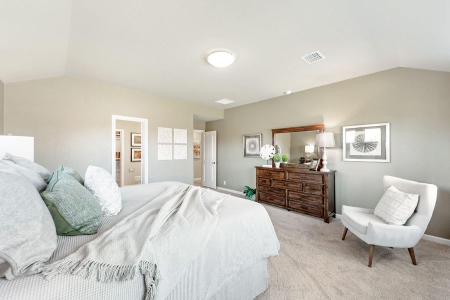 Spacious master bedroom with vaulted ceiling, wood dresser, accent chair, and carpet flooring Spacious master bedroom with vaulted ceiling, wood dresser, accent chair, and carpet flooring