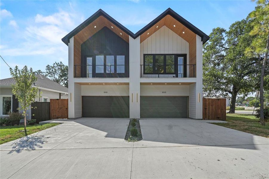 Contemporary home featuring a balcony, a garage, driveway, and a gate