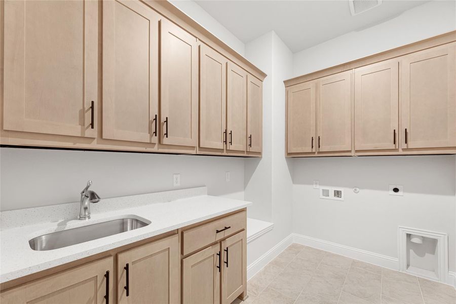 Laundry room with light wood cabinets, utility sink, white countertop, and washer and dryer hookups on tile floor.
