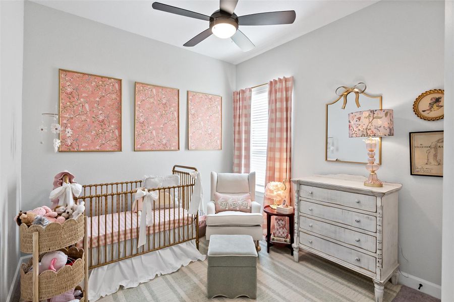 Carpeted bedroom featuring a crib and a ceiling fan