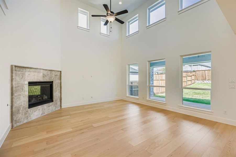 Unfurnished living room with a tile fireplace, light wood-style floors, a high ceiling, and ceiling fan Unfurnished living room with a tile fireplace, light wood-style floors, a high ceiling, and ceiling fan