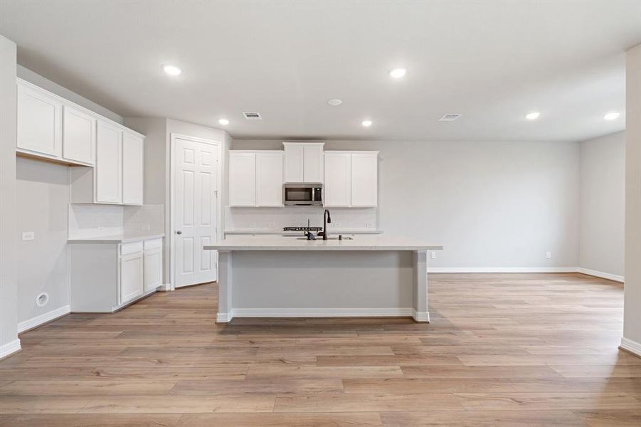 This light and bright kitchen features a large quartz island, white cabinets, a large sink overlooking your family room, recessed lighting, and beautiful backsplash.