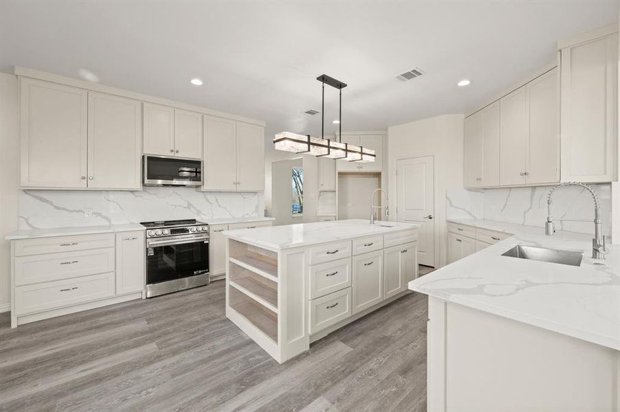 Kitchen with a center island with sink, open shelves, light stone countertops, stainless steel appliances, and backsplash Kitchen with a center island with sink, open shelves, light stone countertops, stainless steel appliances, and backsplash