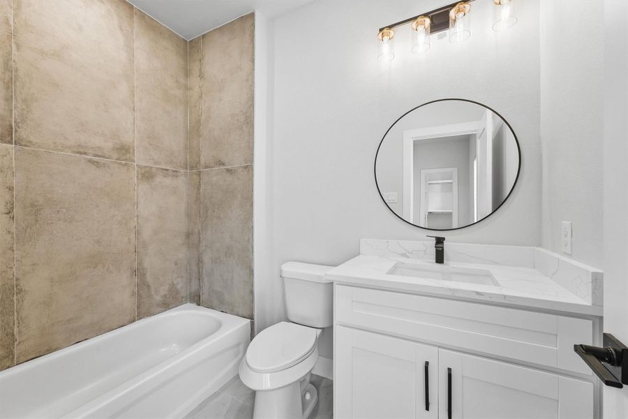 Modern full bathroom featuring a sleek quartz vanity, round mirror, updated lighting, and a tiled tub/shower combo for a clean contemporary finish.