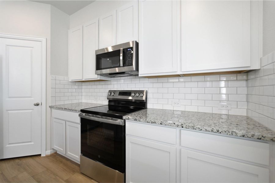 Kitchen featuring stainless steel appliances, white cabinets, light stone counters, light wood finished floors, and tasteful backsplash