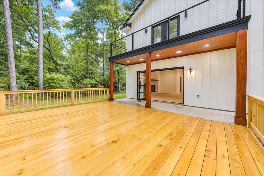 Expansive wooden deck with a modern, open-concept design connects seamlessly to the living area, surrounded by lush trees for a serene outdoor experience.