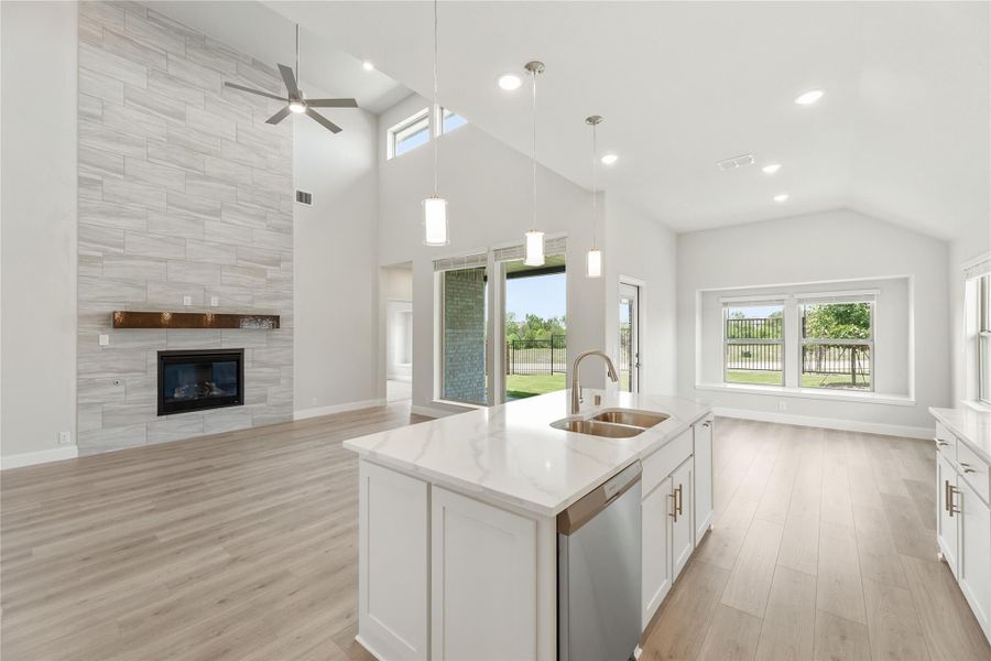 Open-concept kitchen with white island, quartz countertops, and living area with tiled fireplace and vaulted ceiling Open-concept kitchen with white island, quartz countertops, and living area with tiled fireplace and vaulted ceiling