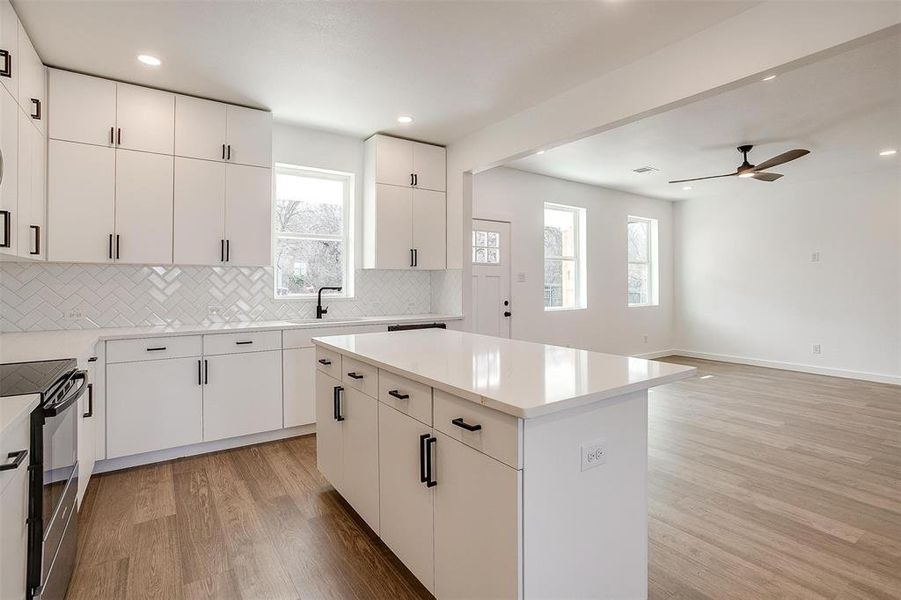 Kitchen featuring white cabinetry, plenty of natural light, light wood-type flooring, a kitchen island, and black electric range oven Kitchen featuring white cabinetry, plenty of natural light, light wood-type flooring, a kitchen island, and black electric range oven