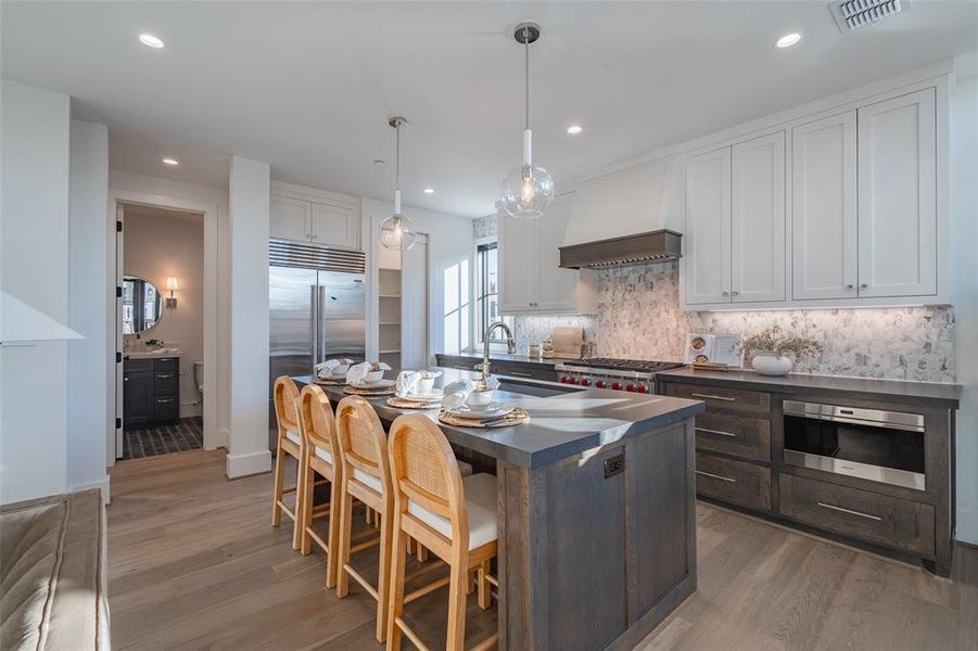 Kitchen with white cabinetry, sink, hanging light fixtures, premium range hood, and appliances with stainless steel finishes