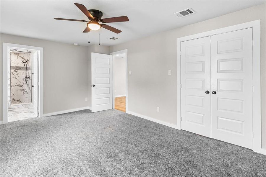 Primary bedroom with carpet flooring, a ceiling fan, ensuite bathroom, and a closet